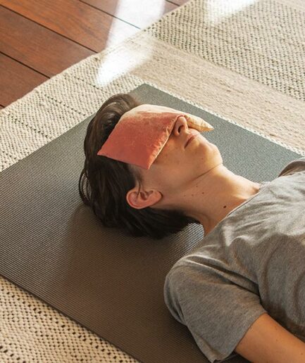 Anne allongée sur un tapis de yoga avec eye-pillow Aura Rouge