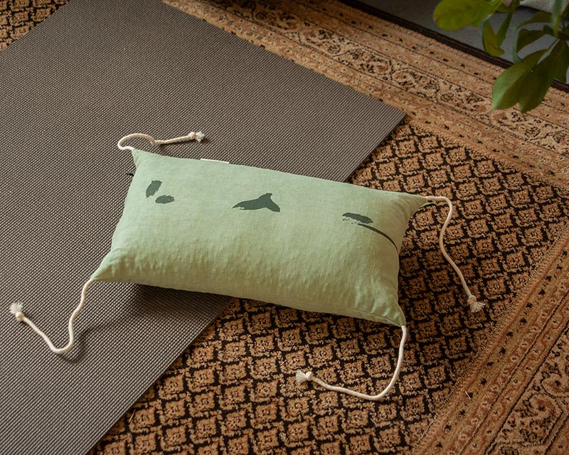 l'oreiller japonais Shodô vert posé au sol d'un salon bohème avec un tapis de yoga bleu