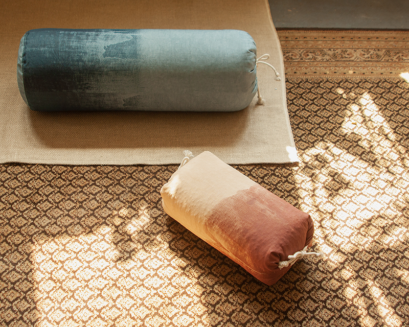 bolster yoga Aura bleu et oreiller japonais Aura rouge posés sur un tapis ocre