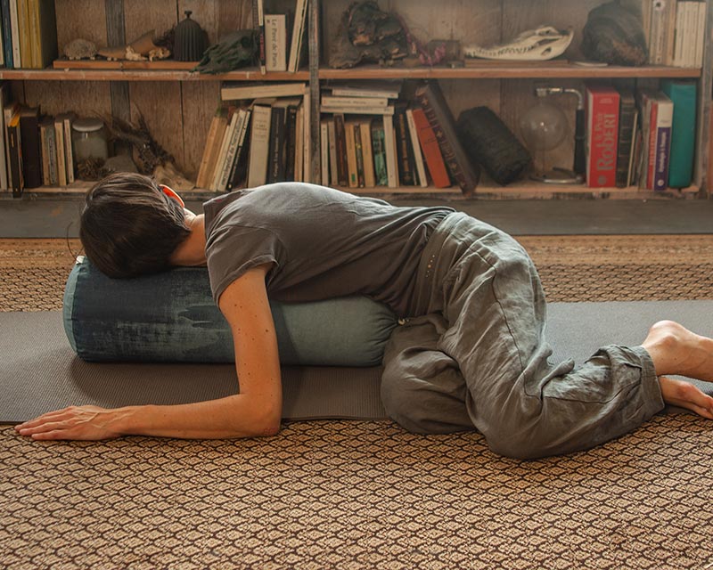 une femme fait du yoga à la maison allongée sur un bolster de yoga 