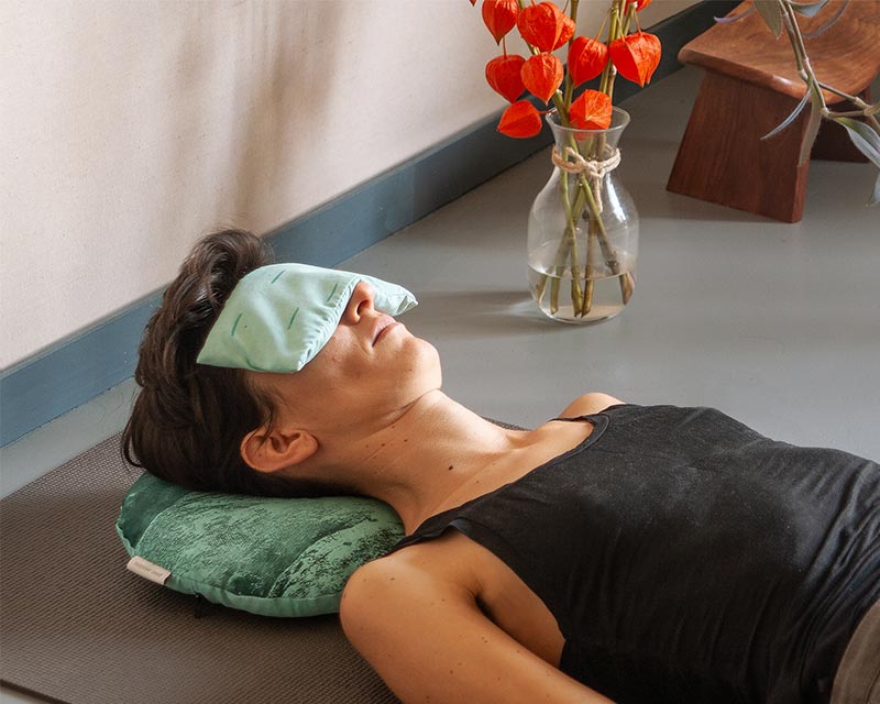 une femme fait du yoga à la maison allongée avec un coussin sur les yeux